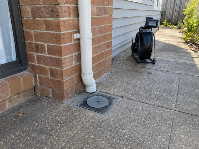 Capped drain inspection opening beside a brick house wall on a concrete path with a coiled camera reel in Kings Langley